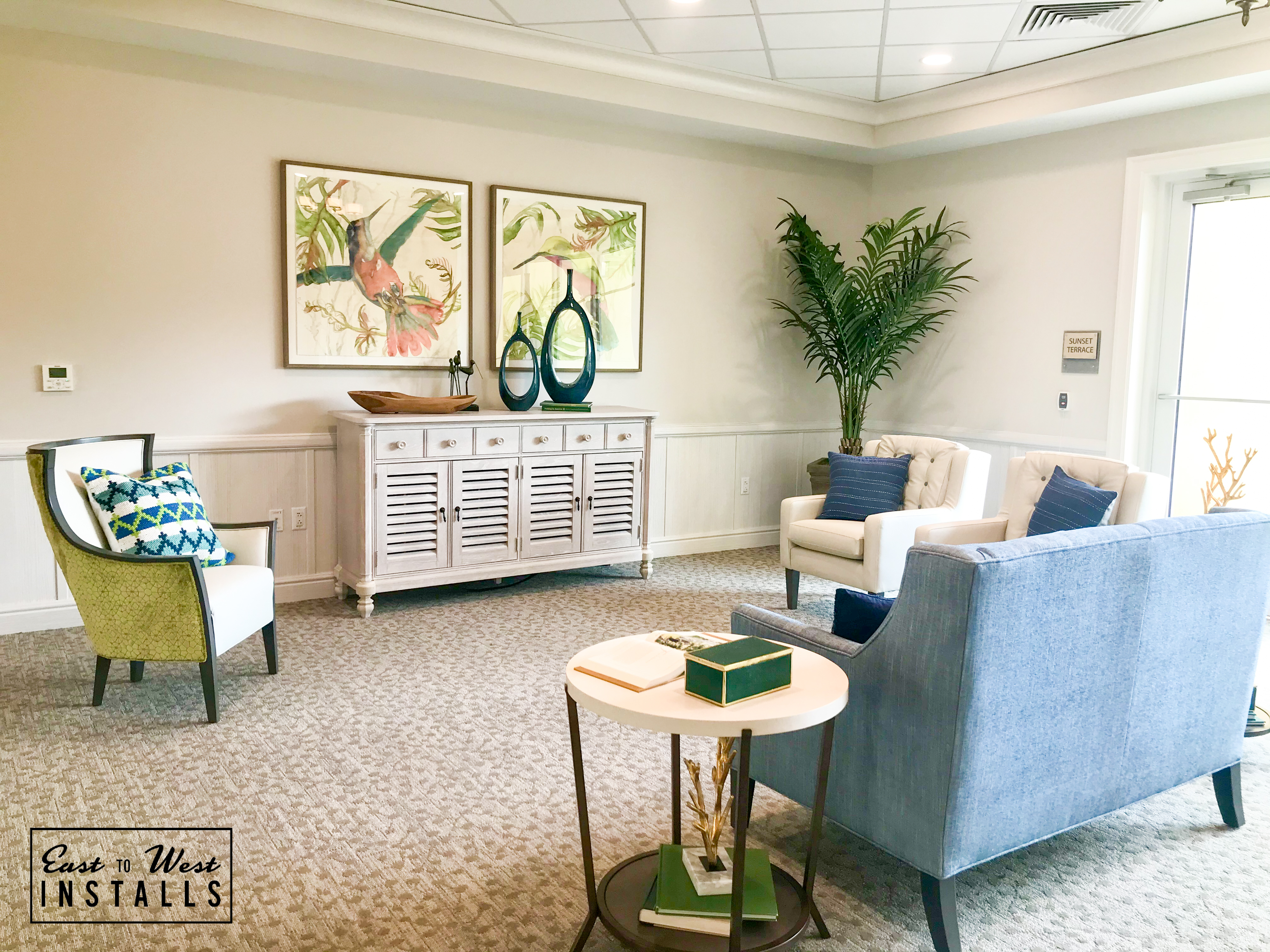 Sunset Terrace lounge — coastal bird artwork, blue settee, palm plant